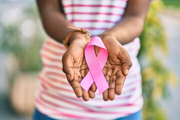 Hands of african american girl holding pink breast cancer ribbon at the park. - Powered by Adobe