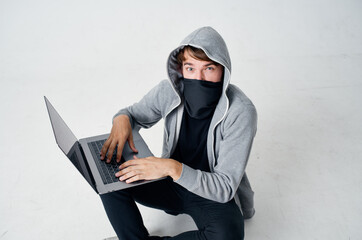 a man in a mask sits on the floor in front of a laptop computer hacking crime