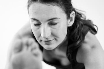 Close-up of a brunette woman in her 30’s with closed eyes practicing yoga at home, doing a two-legged forward bend asana or yoga pose. Horizontal view.