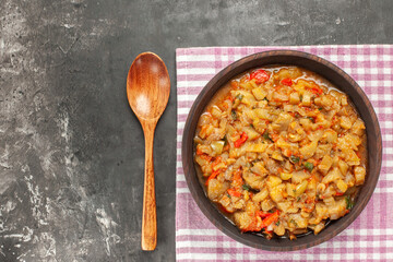 top view roasted eggplant salad in bowl on pink white checkered tablecloth wooden spoon on dark background copy space