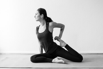 Naklejka na ściany i meble A dark-haired European woman in her 30’s practices yoga at home. Meditation, stretching and mindfulness to achieve physical and spiritual health. Horizontal format.