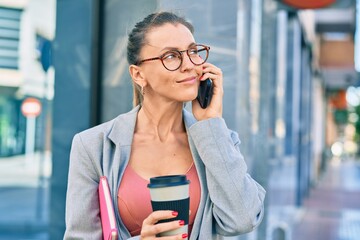 Young blonde businesswoman talking on the smartphone and drinking coffee at the city.