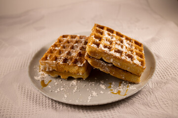 Fresh viennese or belgian waffles on a plate with powdered sugar. Dessert for breakfast.