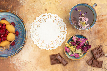 Fototapeta na wymiar Hot herbal tea soft cake with fruits flowers chocolate bars and napkin on mixed color table