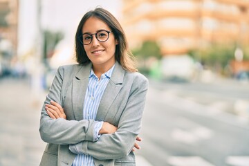 Young hispanic businesswoman with arms crossed smiling happy at the city