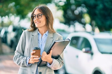 Young hispanic businesswoman drinking coffee holding binder at the city.