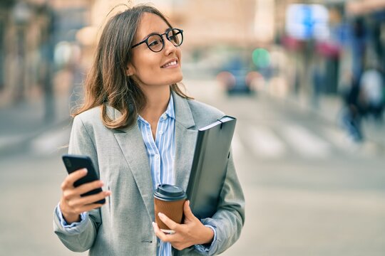 Young hispanic businesswoman using smartphone and drinking take away coffee at the city.