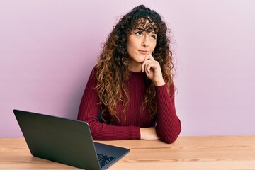 Young hispanic girl working using computer laptop thinking concentrated about doubt with finger on...