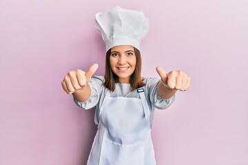 Young beautiful woman wearing professional cook uniform and hat approving doing positive gesture with hand, thumbs up smiling and happy for success. winner gesture.