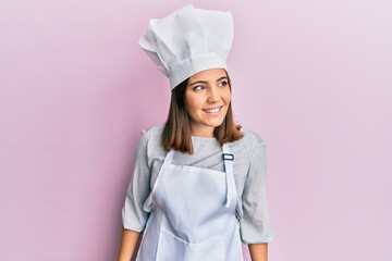 Young beautiful woman wearing professional cook uniform and hat looking away to side with smile on face, natural expression. laughing confident.