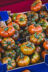 Beautiful red and green tomatoes in a cardboard box in the vendor's stall in italian food market on the street. Ripe, plump organic vegetables for healthy eating. Sunny natural light.