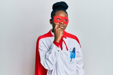 Young african american woman wearing doctor uniform and super hero costume thinking concentrated...