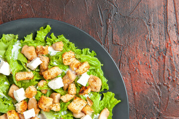 top half view caesar salad on oval plate on dark red background