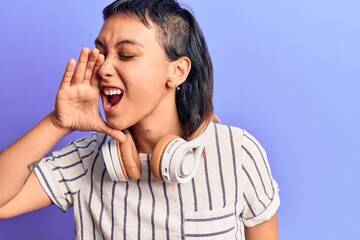 Young woman listening to music using headphones shouting and screaming loud to side with hand on mouth. communication concept.