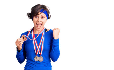 Beautiful young woman with short hair wearing winner medals screaming proud, celebrating victory and success very excited with raised arms