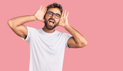 Young hispanic man wearing casual clothes and glasses smiling cheerful playing peek a boo with hands showing face. surprised and exited