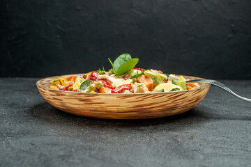 side close view of bowl of vegetable salad with fork on side on dark grey table on dark grey background
