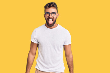 Young hispanic man wearing casual clothes and glasses sticking tongue out happy with funny expression. emotion concept.