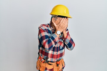 Senior hispanic man wearing handyman uniform with sad expression covering face with hands while crying. depression concept.