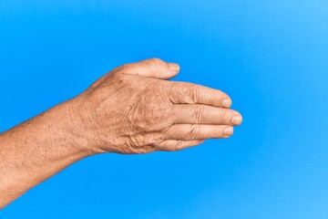 Hand of senior hispanic man over blue isolated background stretching and reaching with open hand for handshake, showing back of the hand