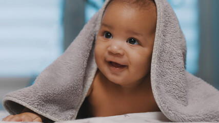 Adorable dark skin baby covered with towel having fun tummy time. High quality photo