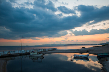 Sunset view of small fishing boats moored on Athens pier with reflections of cloudy sky in the water. Greece.