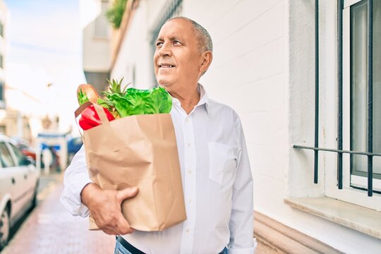 Senior man smiling happy holding paper bag with food walking at the city.
