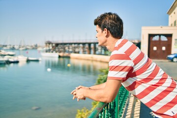 Fototapeta premium Young caucasian man smiling happy leaning on the balustrade at river