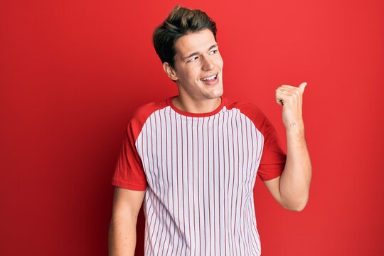 Handsome caucasian man wearing baseball uniform pointing thumb up to the side smiling happy with open mouth