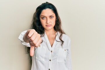 Beautiful middle eastern woman wearing casual clothes looking unhappy and angry showing rejection and negative with thumbs down gesture. bad expression.