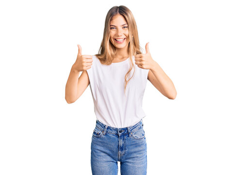 Beautiful caucasian woman with blonde hair wearing casual white tshirt success sign doing positive gesture with hand, thumbs up smiling and happy. cheerful expression and winner gesture.