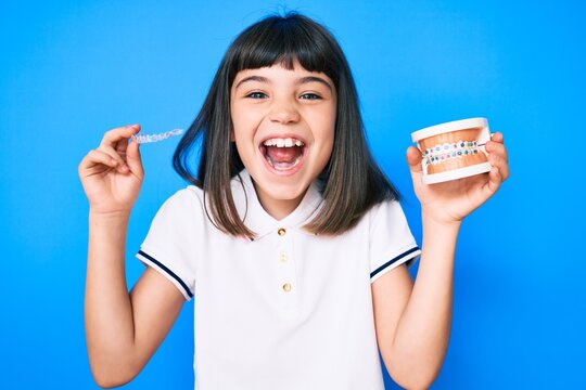 Young little girl with bang holding invisible aligner orthodontic and braces smiling and laughing hard out loud because funny crazy joke.
