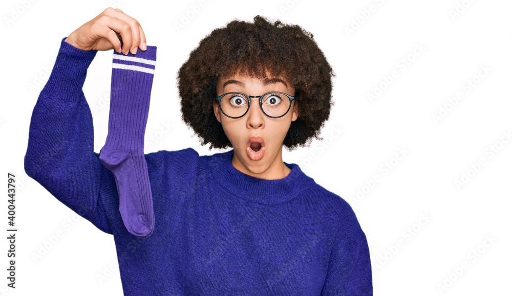 Wall mural Young hispanic girl holding sporty sock scared and amazed with open mouth for surprise, disbelief face