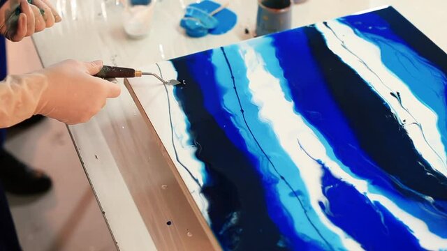 The hand of the artist in a glove makes stains on the paint of the painting in blue with the tool. Free expression of the master's creative imagination. Working with liquid paint on a hard surface.