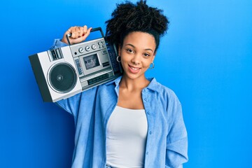 Young african american girl holding boombox, listening to music looking positive and happy standing...