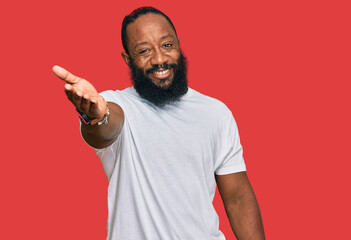 Young african american man wearing casual white tshirt smiling friendly offering handshake as greeting and welcoming. successful business.