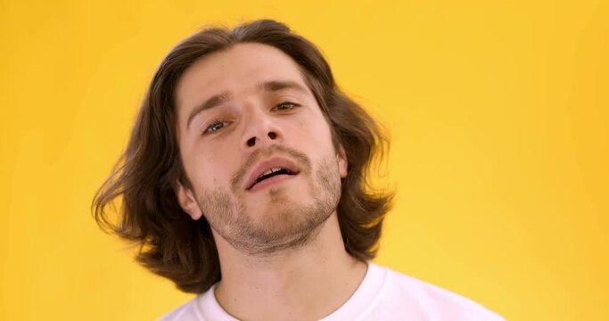 Close up portrait of young arrogant guy looking snooty to camera, preening his hair, yellow studio background