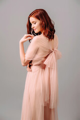 Fototapeta premium Elegant salmon dress. Beautiful peach chiffon evening gown. Studio portrait of young brunette woman. Bridesmaid dresses.