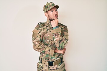 Young caucasian man wearing camouflage army uniform with hand on chin thinking about question, pensive expression. smiling with thoughtful face. doubt concept.