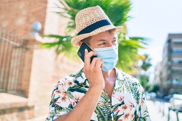 Caucasian handsome man smiling happy outdoors talking on the phone wearing coronavirus safety mask