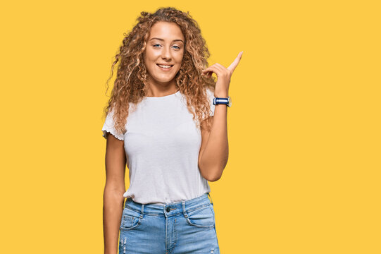 Beautiful caucasian teenager girl wearing casual white tshirt with a big smile on face, pointing with hand finger to the side looking at the camera.