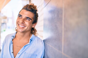Naklejka na ściany i meble Young handsome hispanic man smiling happy leaning on the wall at street of city