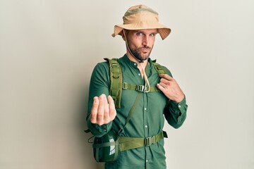 Fototapeta premium Handsome man with beard wearing explorer hat and backpack doing money gesture with hands, asking for salary payment, millionaire business
