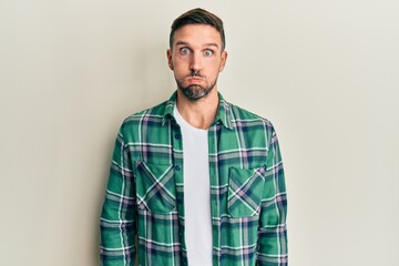 Handsome man with beard wearing casual clothes puffing cheeks with funny face. mouth inflated with air, crazy expression.