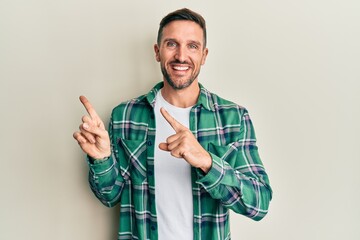 Handsome man with beard wearing casual clothes smiling and looking at the camera pointing with two hands and fingers to the side.