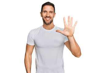 Naklejka premium Handsome man with beard wearing casual white t shirt showing and pointing up with fingers number five while smiling confident and happy.