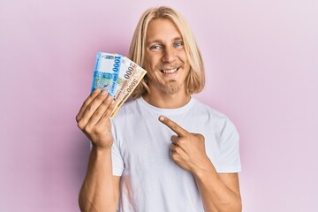 Caucasian young man with long hair holding hungarian forint banknotes smiling happy pointing with hand and finger