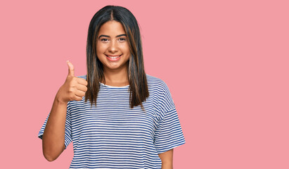 Young latin girl wearing casual clothes doing happy thumbs up gesture with hand. approving expression looking at the camera showing success.