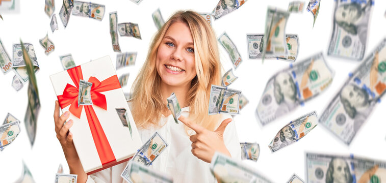 Young beautiful blonde woman holding gift pointing finger to one self smiling happy and proud