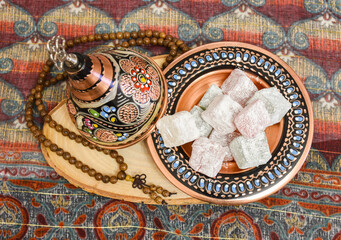 Traditional Turkish delight (blasting cartridge) in traditional hand made cooper bowl with prayer-beads on wood. Fabric background.